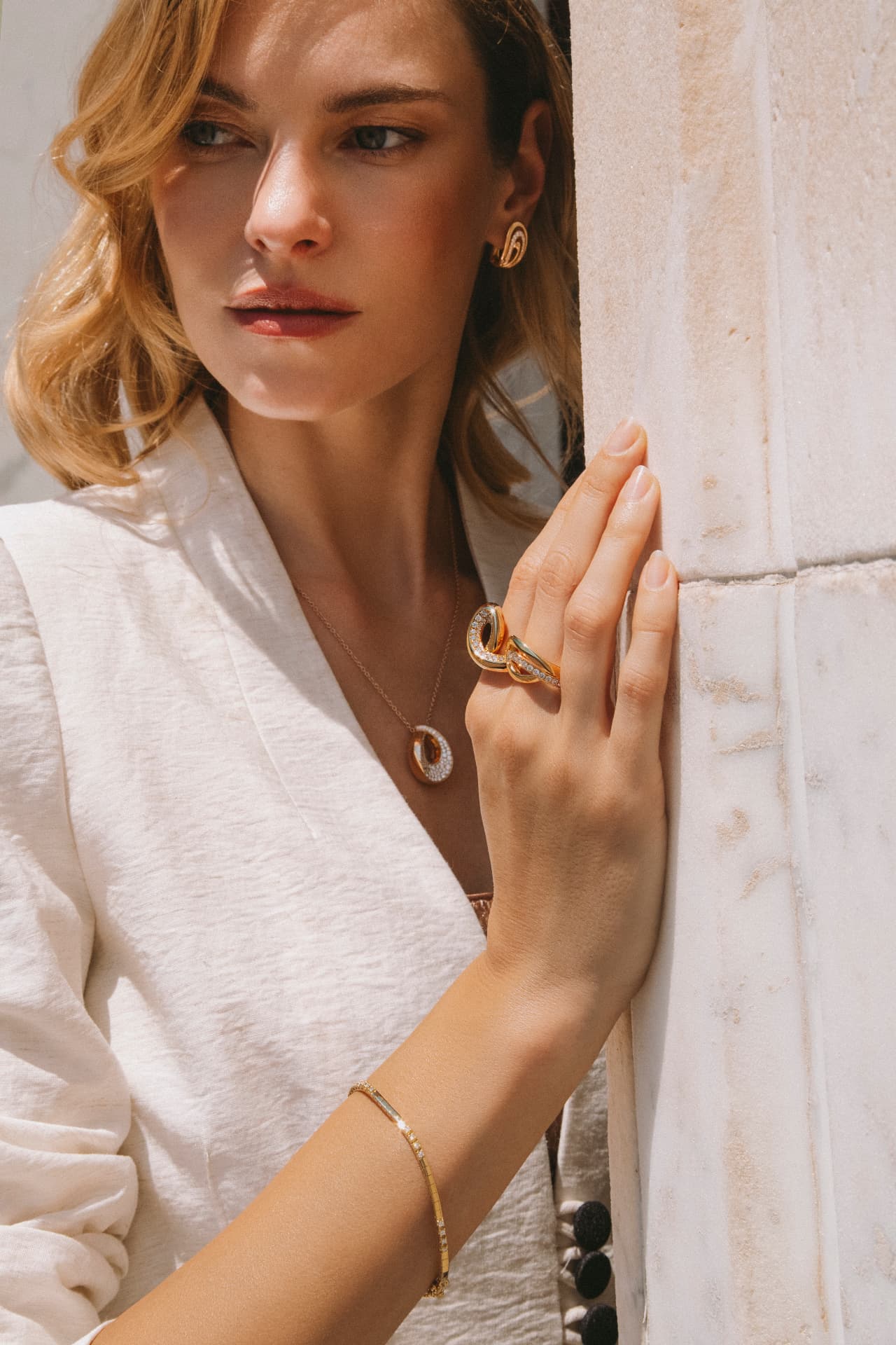 Model wearing Italian gold jewelry — earrings, necklace, rings and bracelet — in an ivory suit